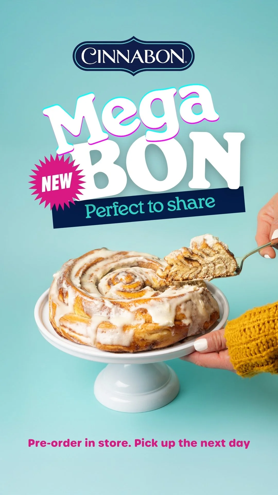 A cinnamon roll with white icing on a white cake stand. A hand in a yellow sweater is holding a fork with a piece of the cinnamon roll. Megabon - Cinnabon Cake
