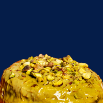 Close-up of a Cinnabon  pistachio-topped dessert with yellow glaze against a dark blue background.