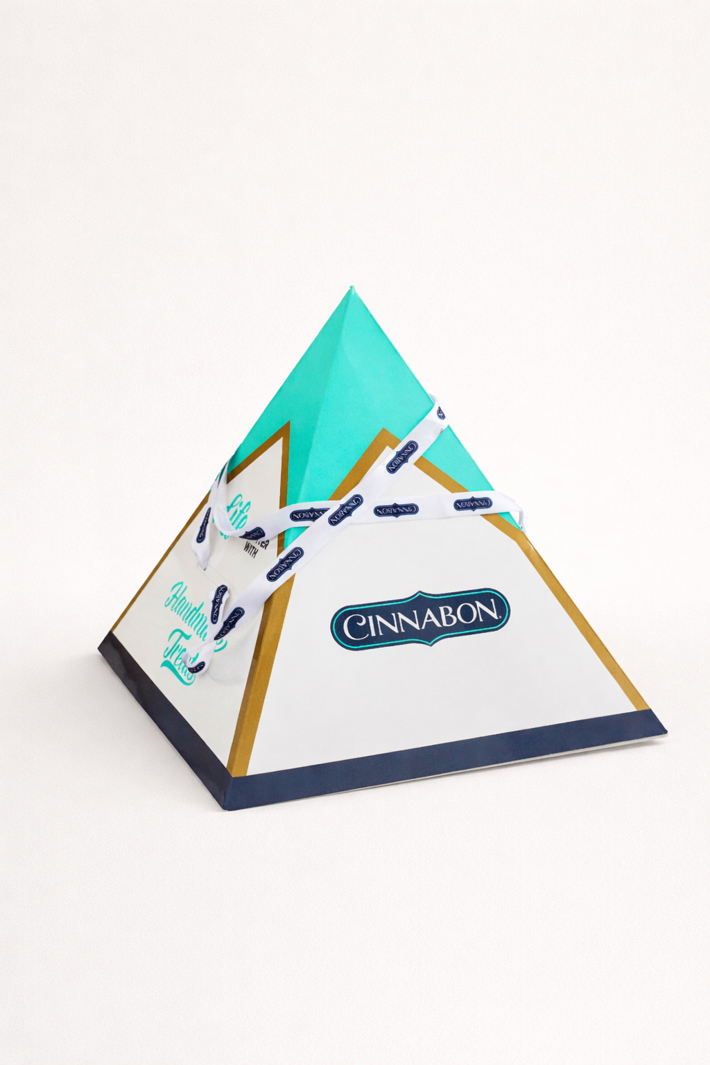 Pyramid-shaped Cinnabon gift box on a clean neutral background, featuring turquoise and white packaging with a branded ribbon.