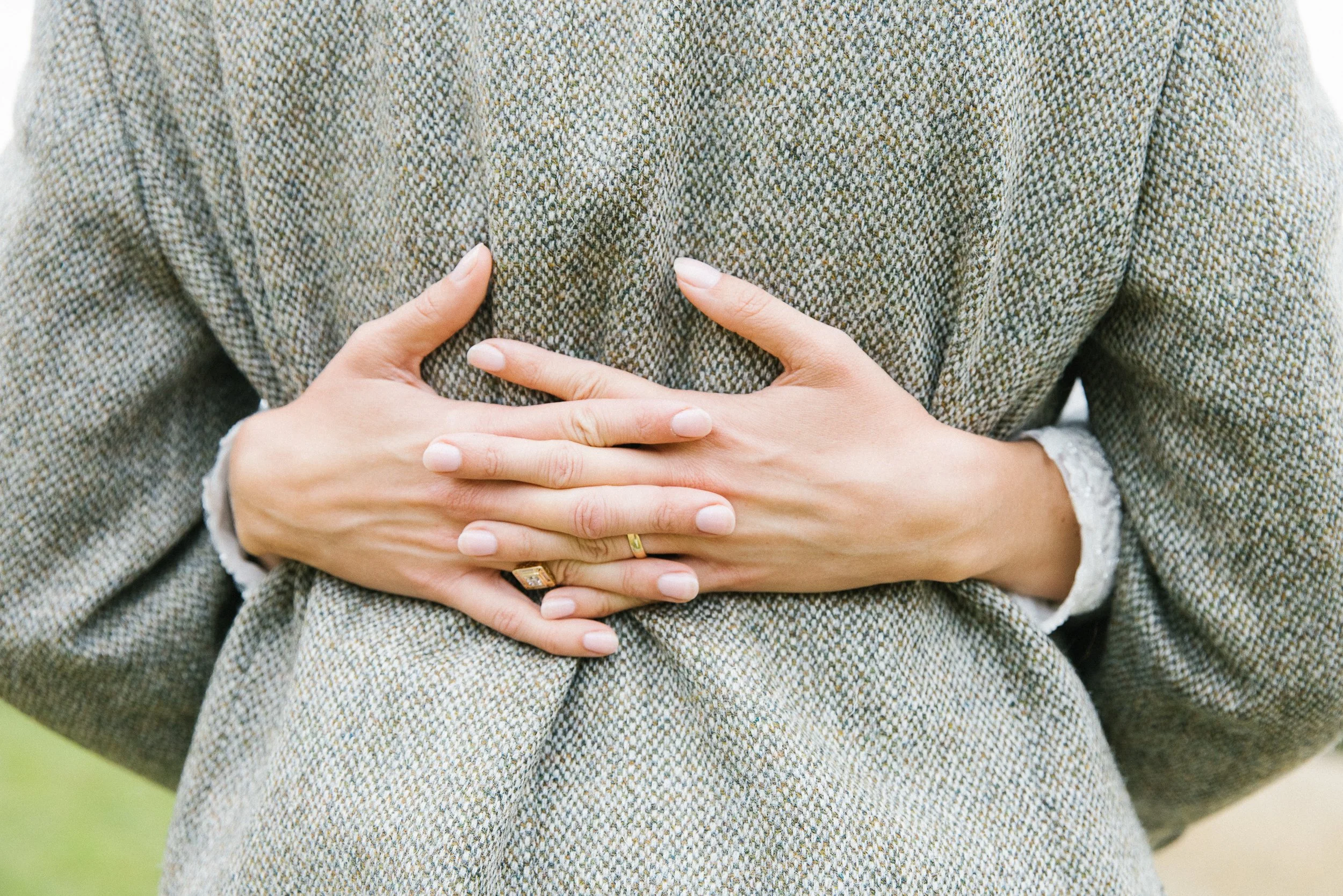 Person holding their hands over their chest, wearing a gray plaid blazer.