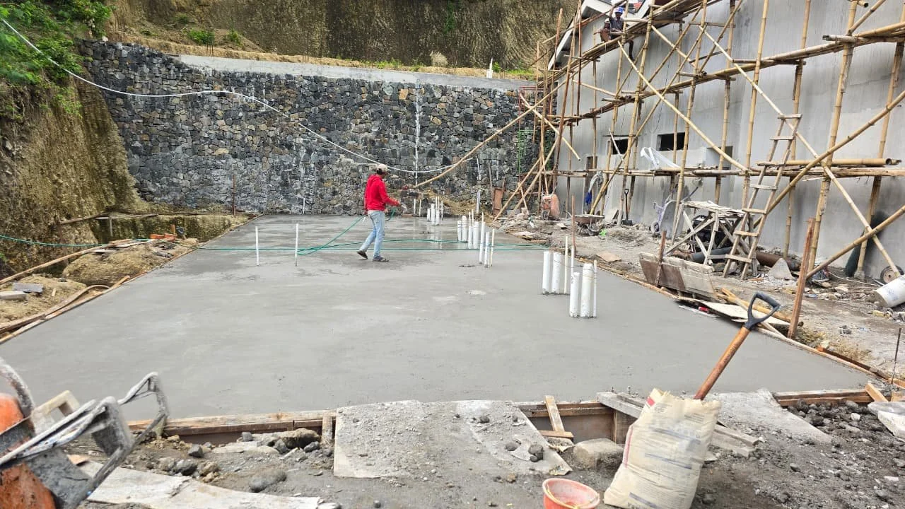 Construction site with workers installing a concrete floor, surrounded by scaffolding and retaining wall.