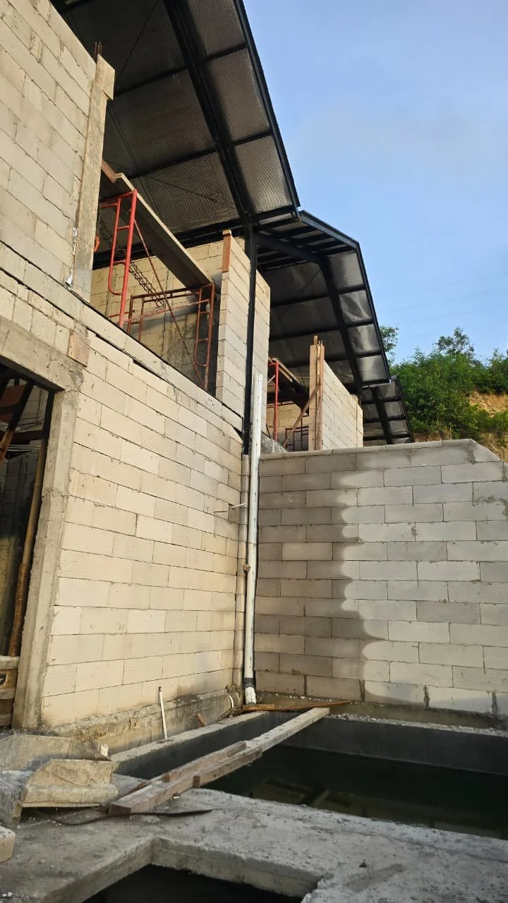 Construction site with unfinished brick walls, scaffolding, and a sloped metal roof structure.