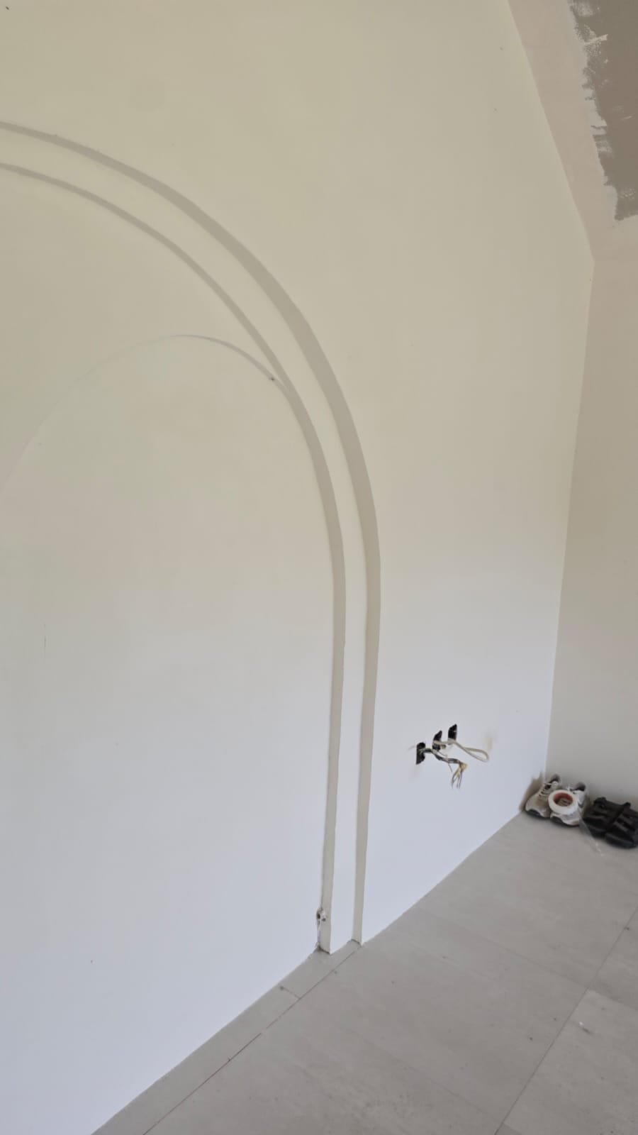 Interior wall with decorative arch molding, electrical outlets and wires, and construction tools on the floor.