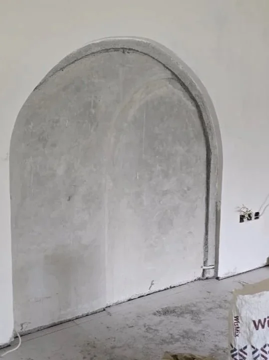 Unfinished interior wall with an arched doorway and exposed electrical wiring.