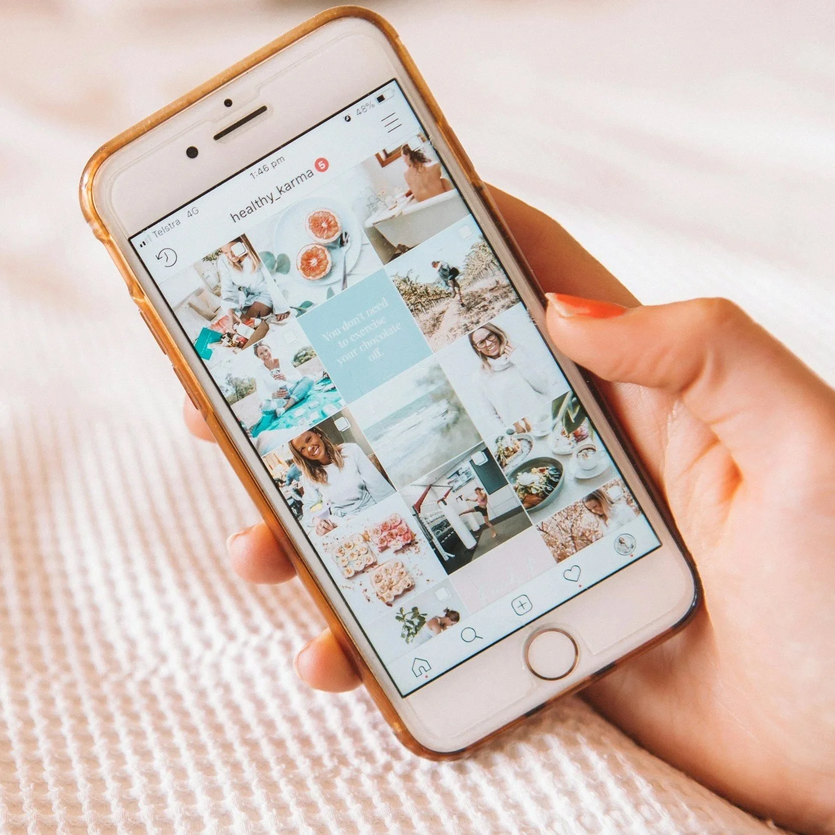 Close-up of a person's hand holding a smartphone displaying an Instagram profile with various photos of food, outdoor activities, and people.