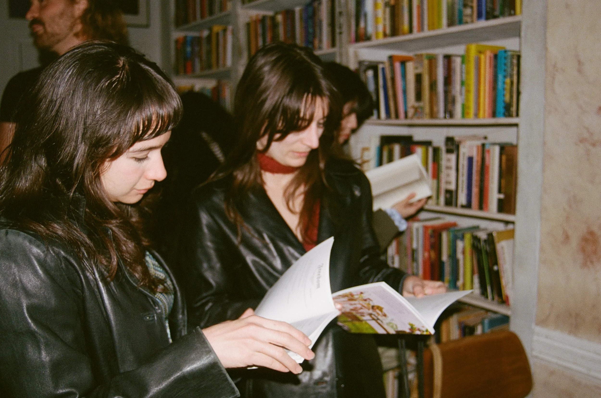 Three women reading books in a bookstore or library, with bookshelves in the background.