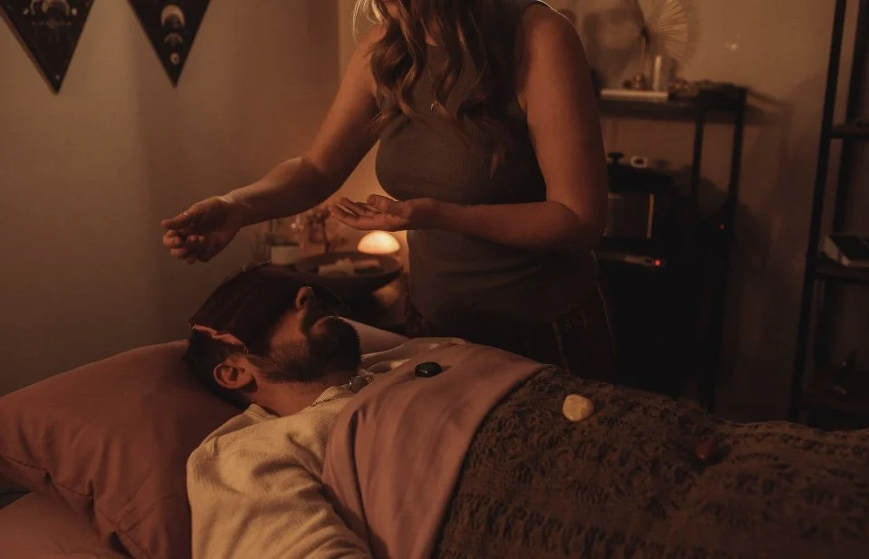 A woman appears to be giving a digital healing or energy transfer to a man lying in bed at night in a cozy, dimly-lit room.