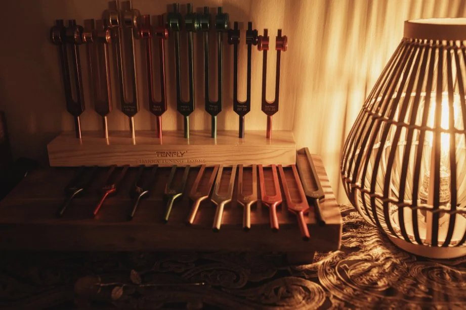 A wooden stand holding metal screwdrivers with black, red, green, and copper handles, accompanied by a decorative woven lamp emitting warm light, placed on a textured surface with a curtain in the background.