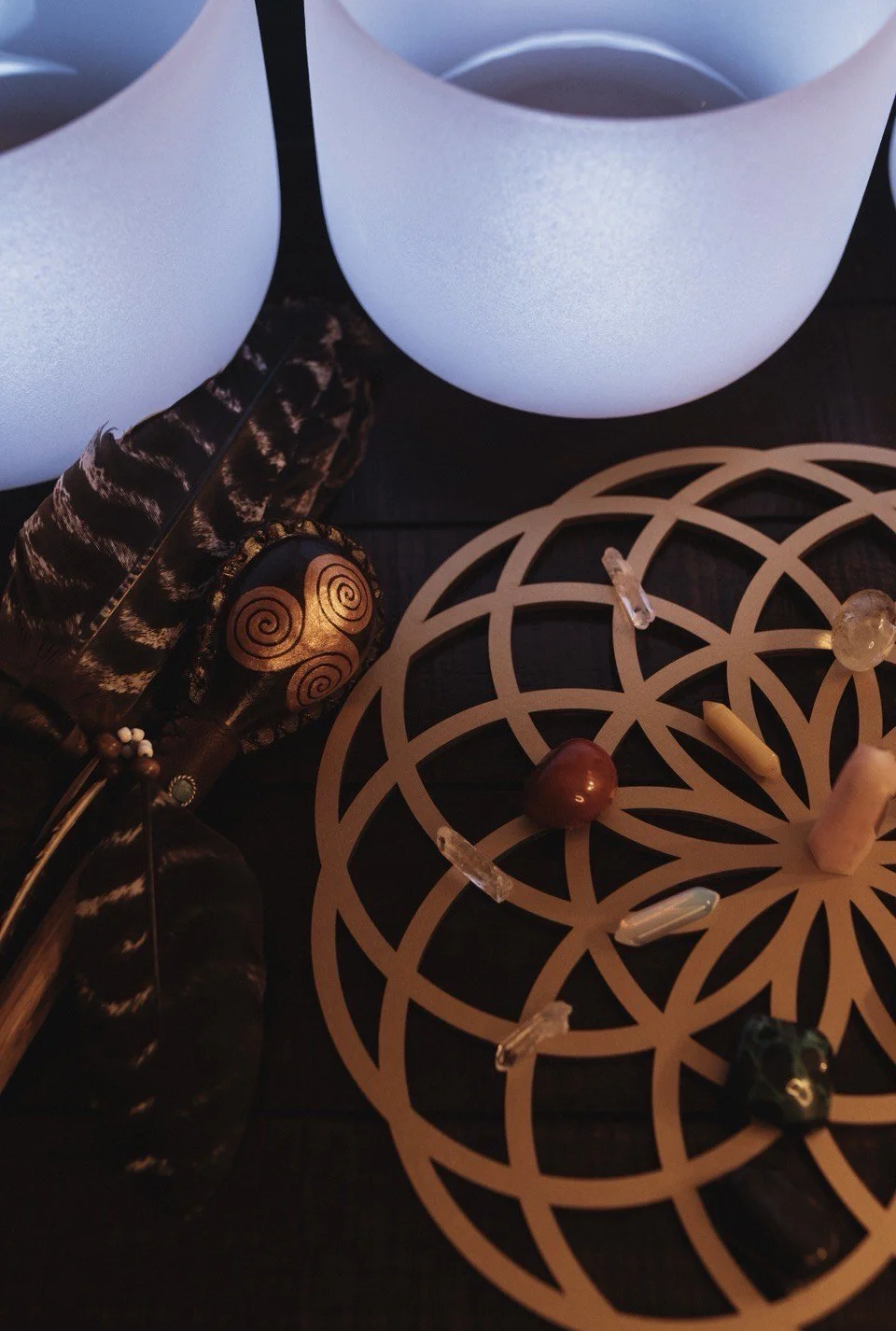 A close-up of a crystal grid with various stones on an intricate geometric pattern, illuminated by three glowing white orbs in the background.