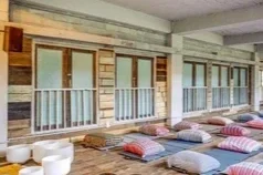Outdoor patio area with wooden deck, white railing, and seating cushions on the ground.
