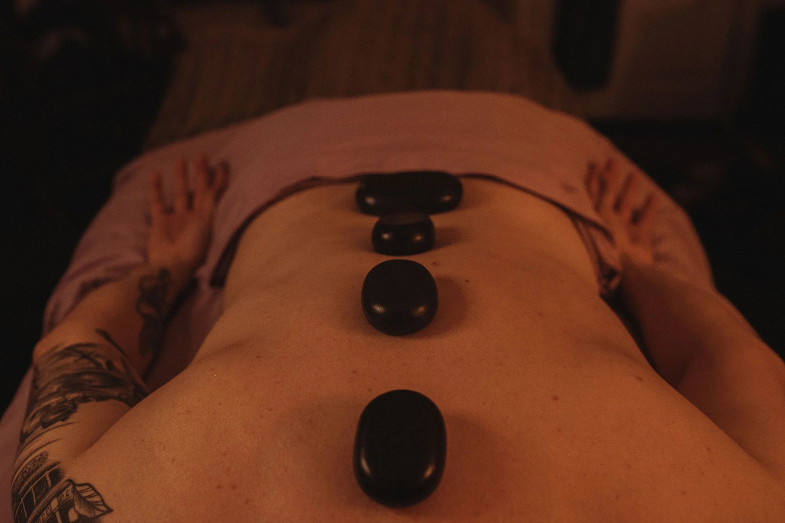 Person lying face up with four black stones placed  along their back during a hot stone massage.