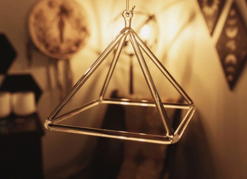 A geometric hanging ornament made of metal rods in the shape of a pyramid, suspended from a ceiling
