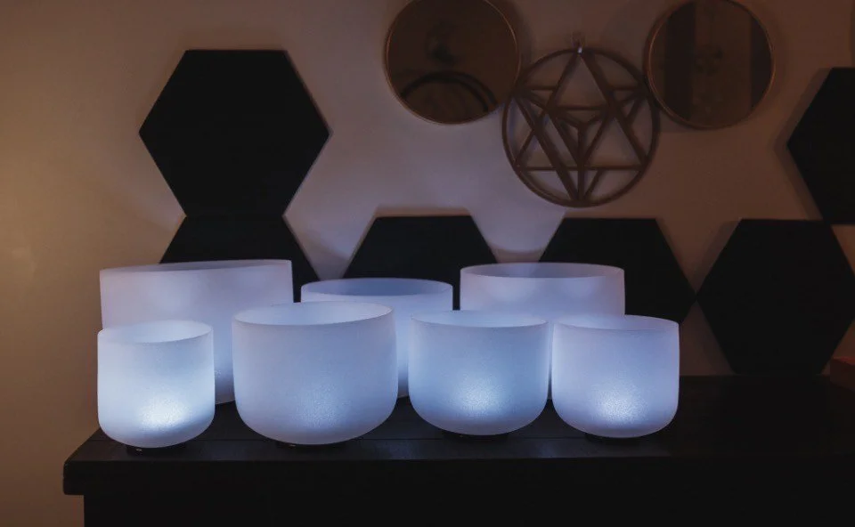 Eight glowing white bowls arranged on a dark surface against a dark wall with geometric decor.
