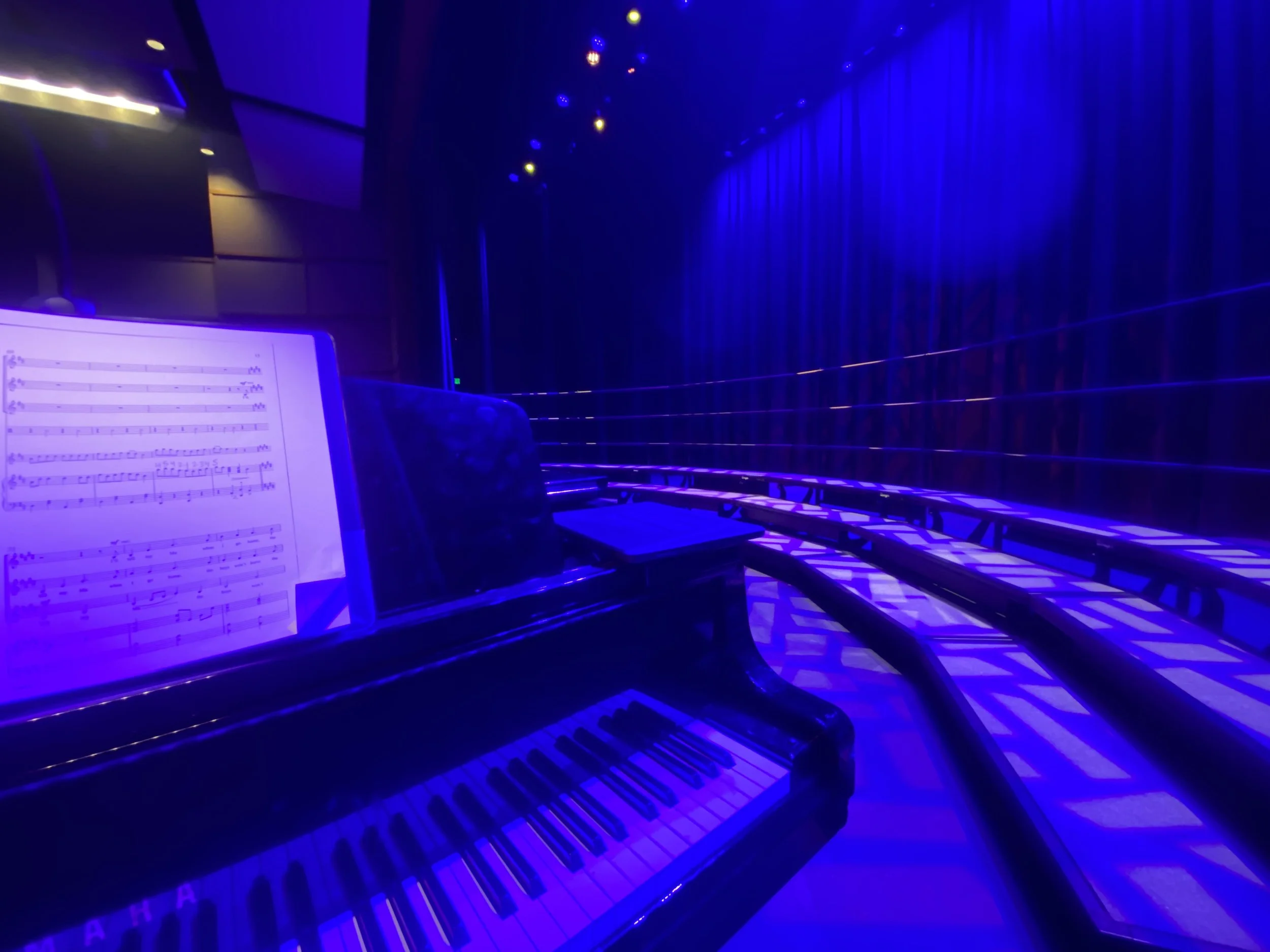 A dimly lit music venue with a piano and sheet music illuminated by blue and purple lighting.