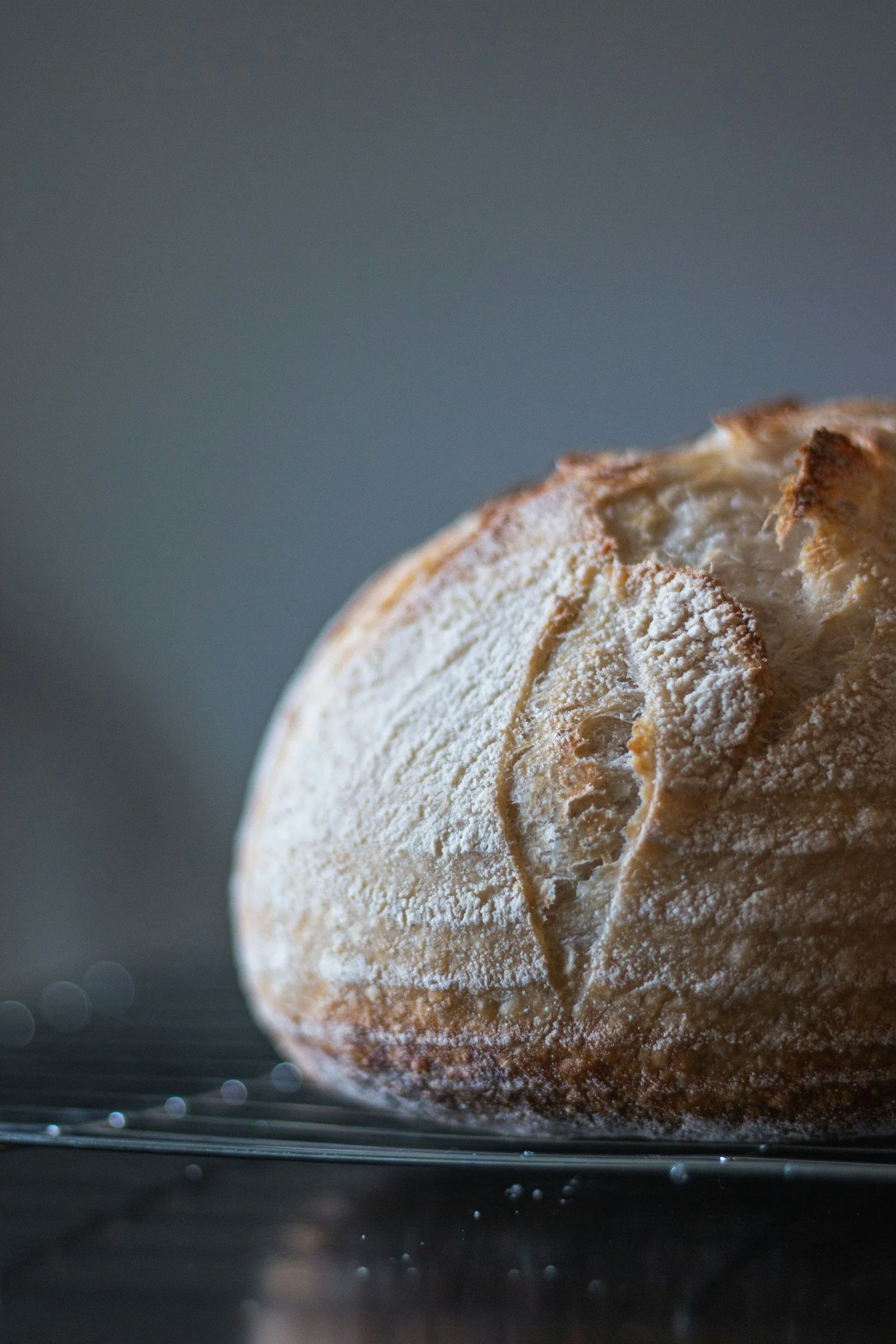 Close-up of a flour-dusted bread loaf on a dark surface with a blurred background.