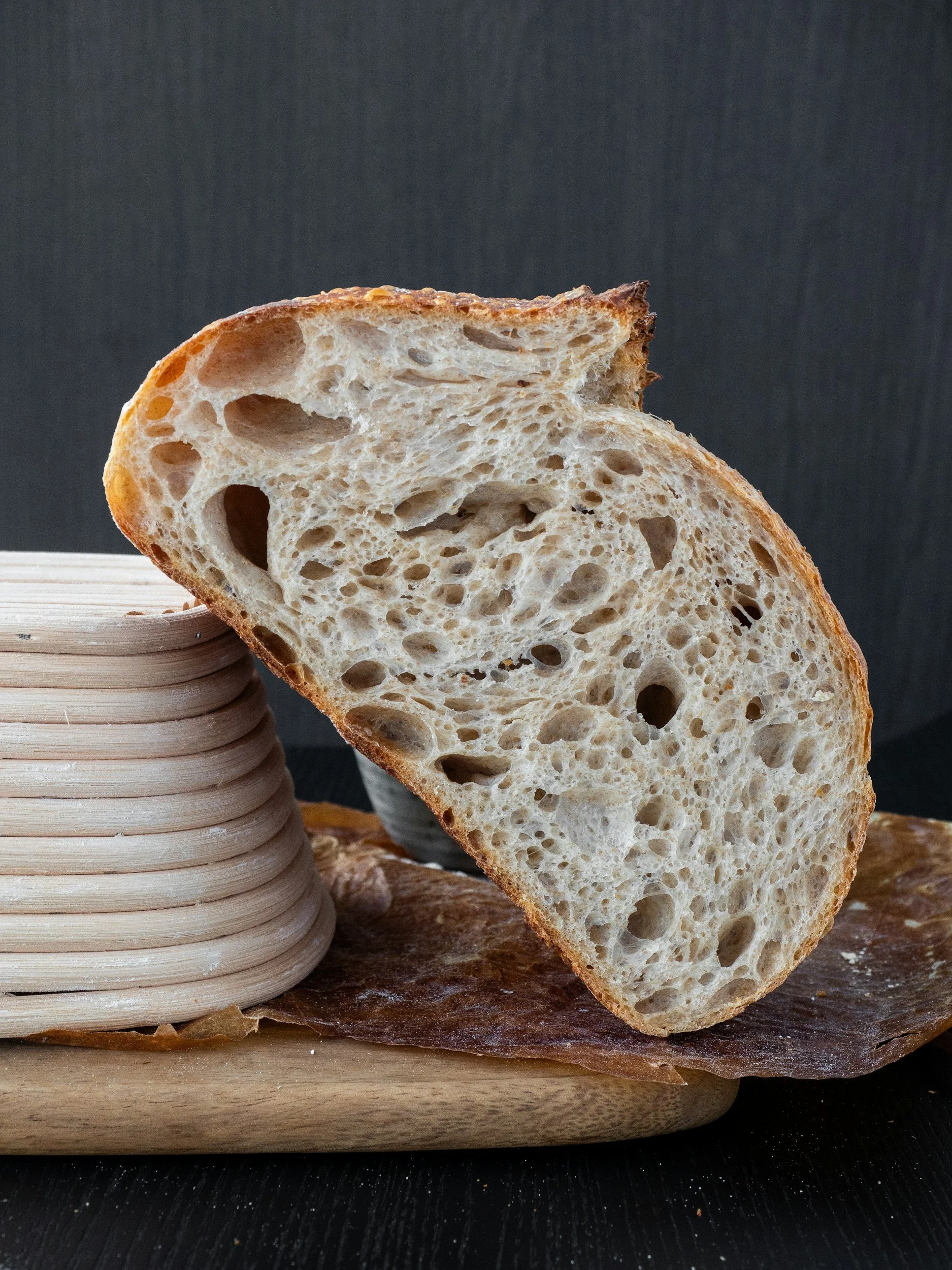 Close-up of sliced rustic sourdough bread with a chewy, airy crumb and a golden crust, resting on a wooden surface with a dark background.