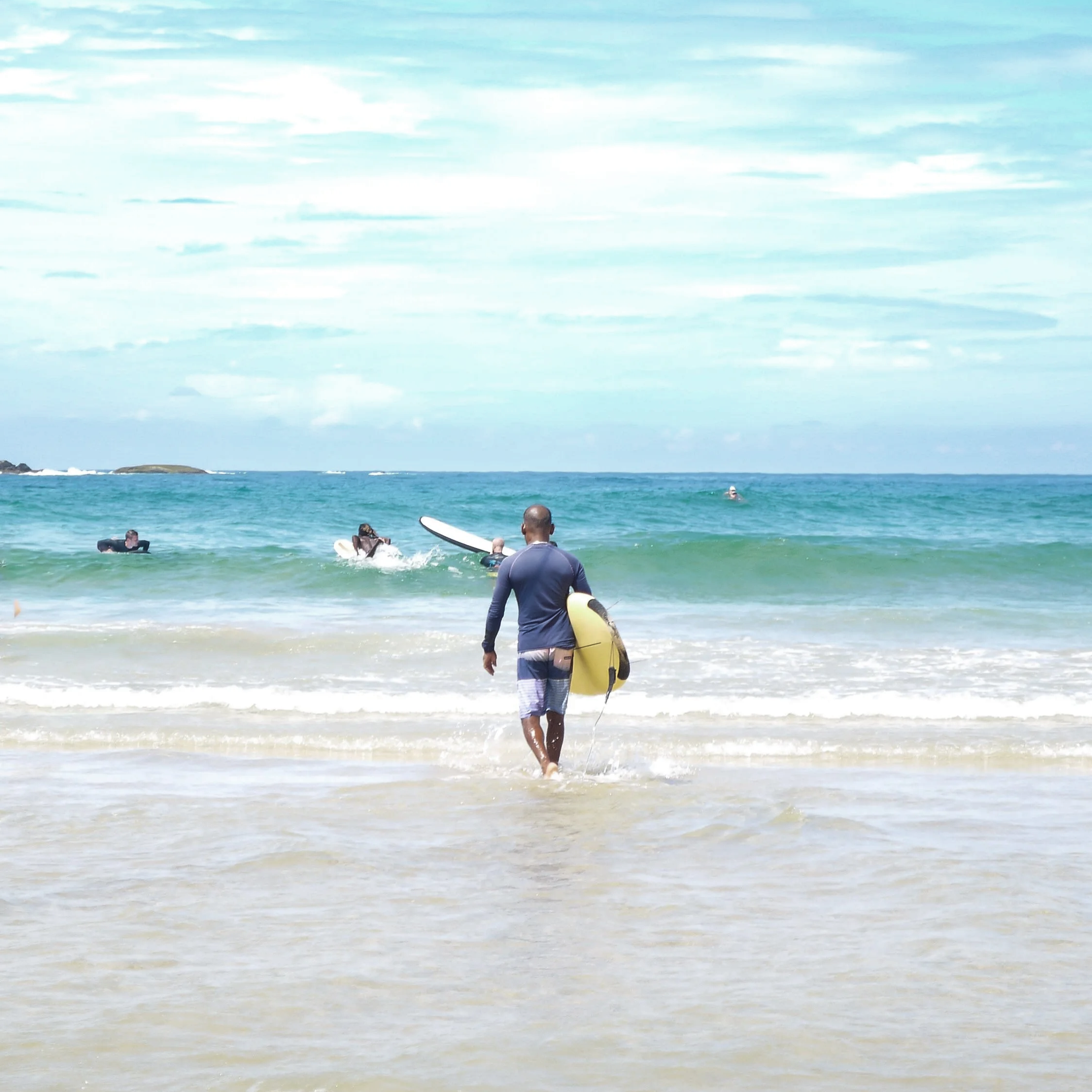 People enjoying the ocean, some are swimming and others are sitting on the shore, with a cloudy sky overhead.