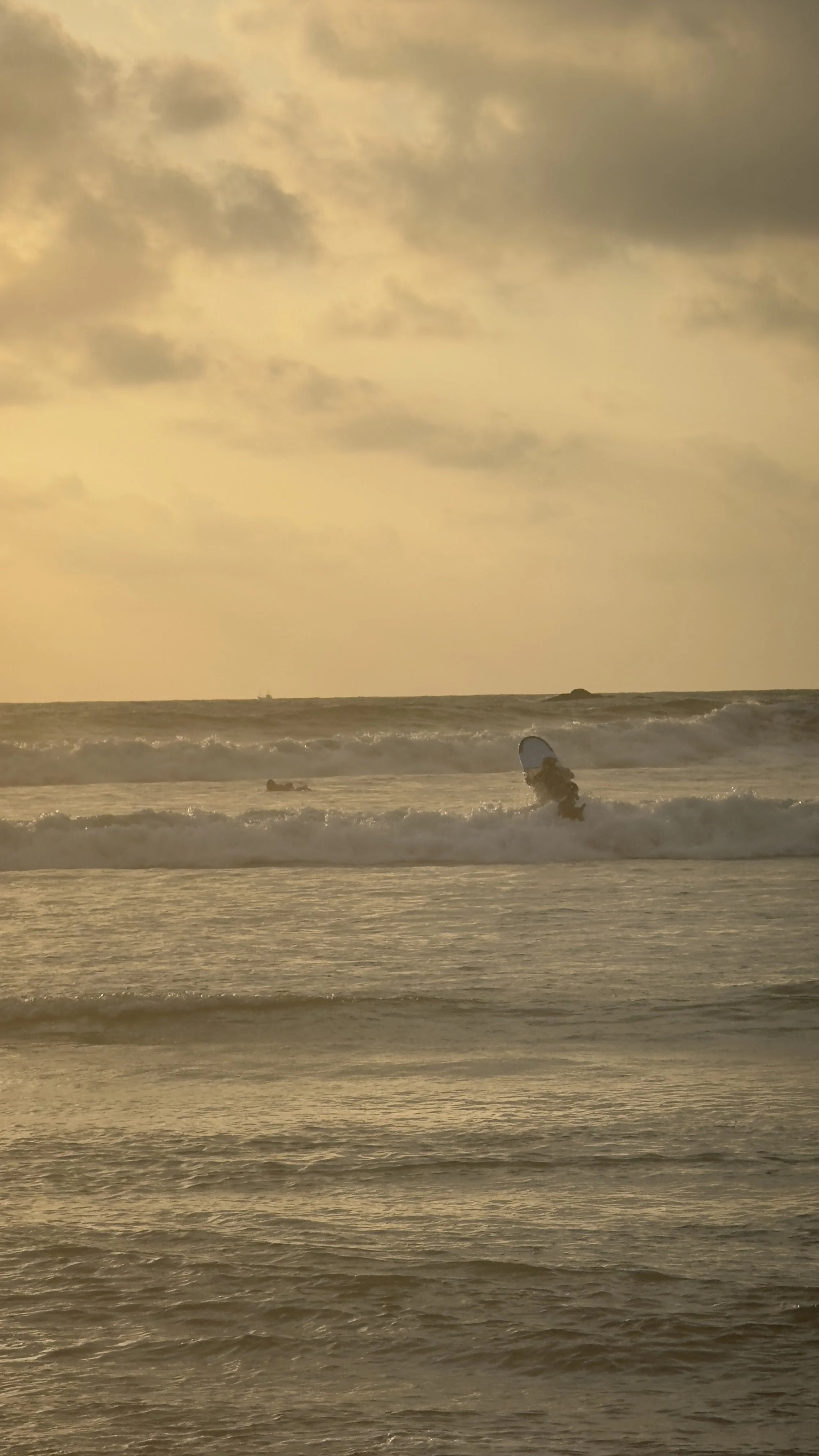 A person surfing in the ocean during sunset, with cloudy sky and waves surrounding them.