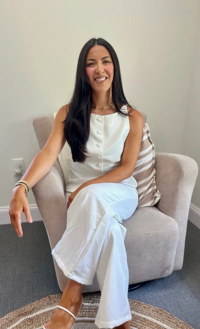 Portrait of a woman with long dark hair, smiling, wearing a black turtleneck against a plain white background.