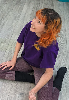 Close-up of a man with black curly hair, a beard, wearing clear round glasses and a black sweater, looking slightly to the side with a neutral expression.