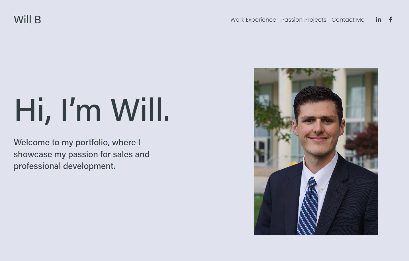 Photograph of a young man in a suit and tie smiling outdoors in front of a modern building
