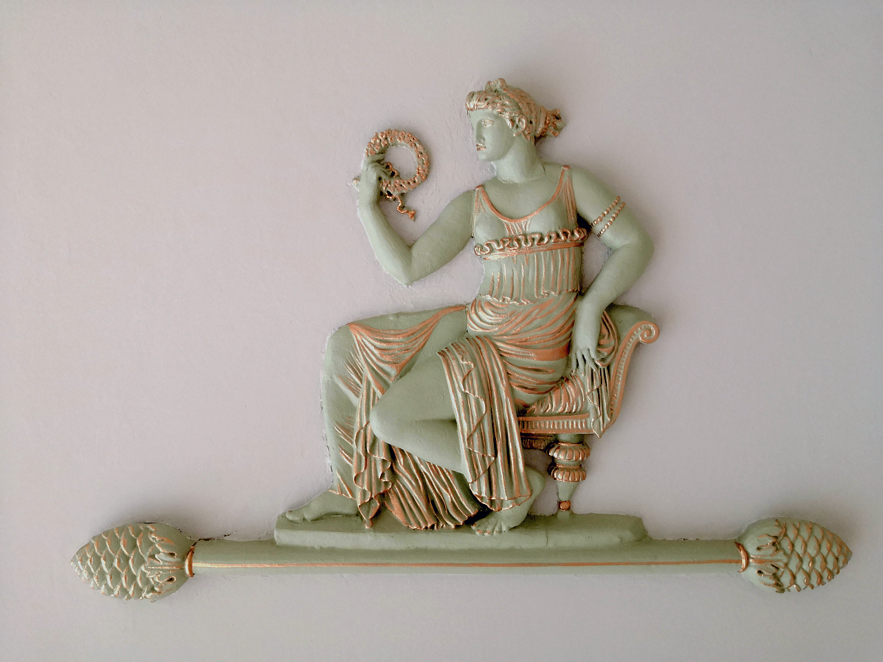 Een sculptuur van een vrouw in klassieke kleding zittend op een bank, met een slang in haar hand.