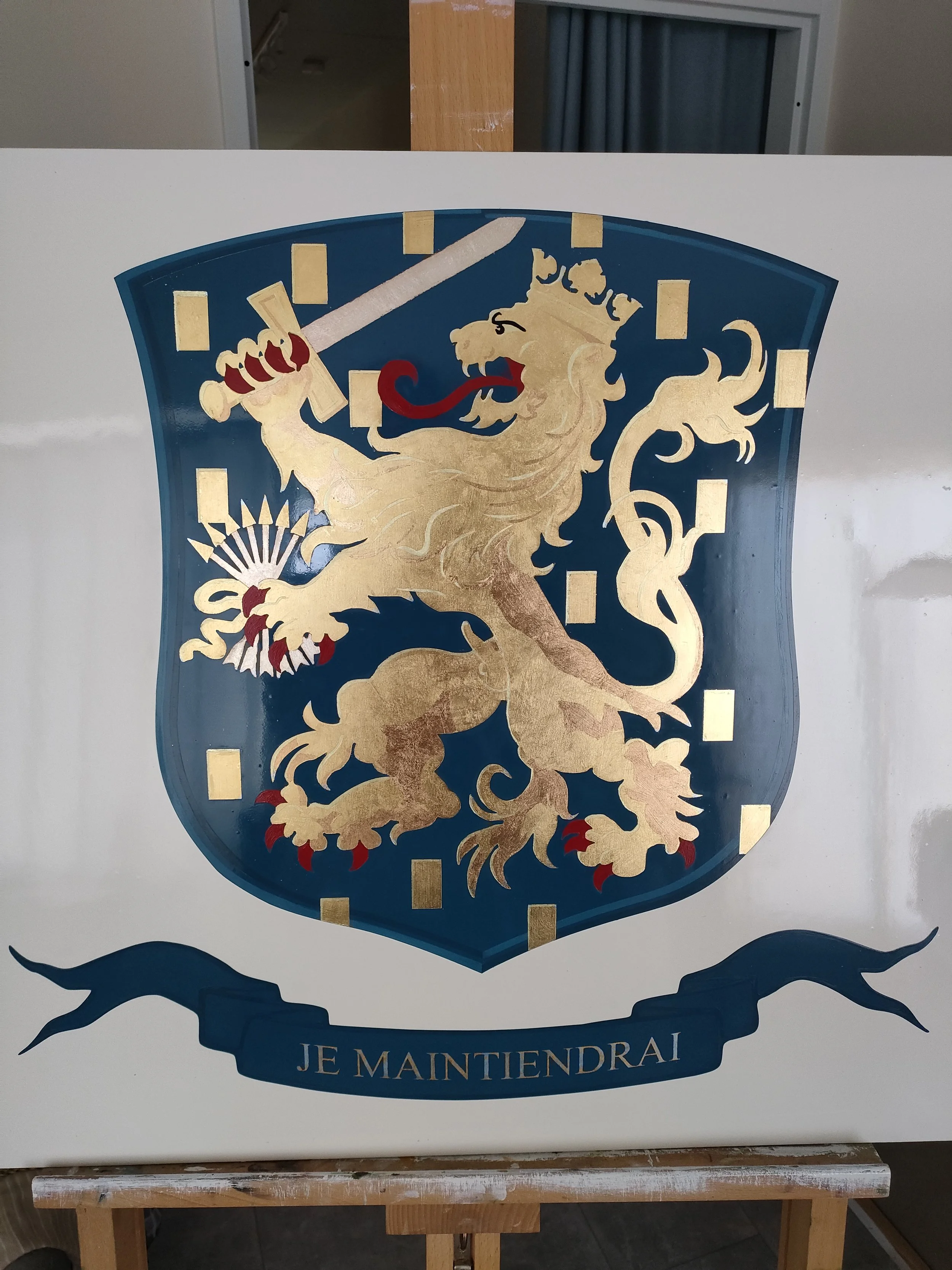 Een schild met een goudkleurige leeuw die een zwaard vasthoudt, op een blauwe achtergrond met goudkleurige blokken, en een blauwe band onderaan met de tekst 'JE MAINTIENDRAI'.