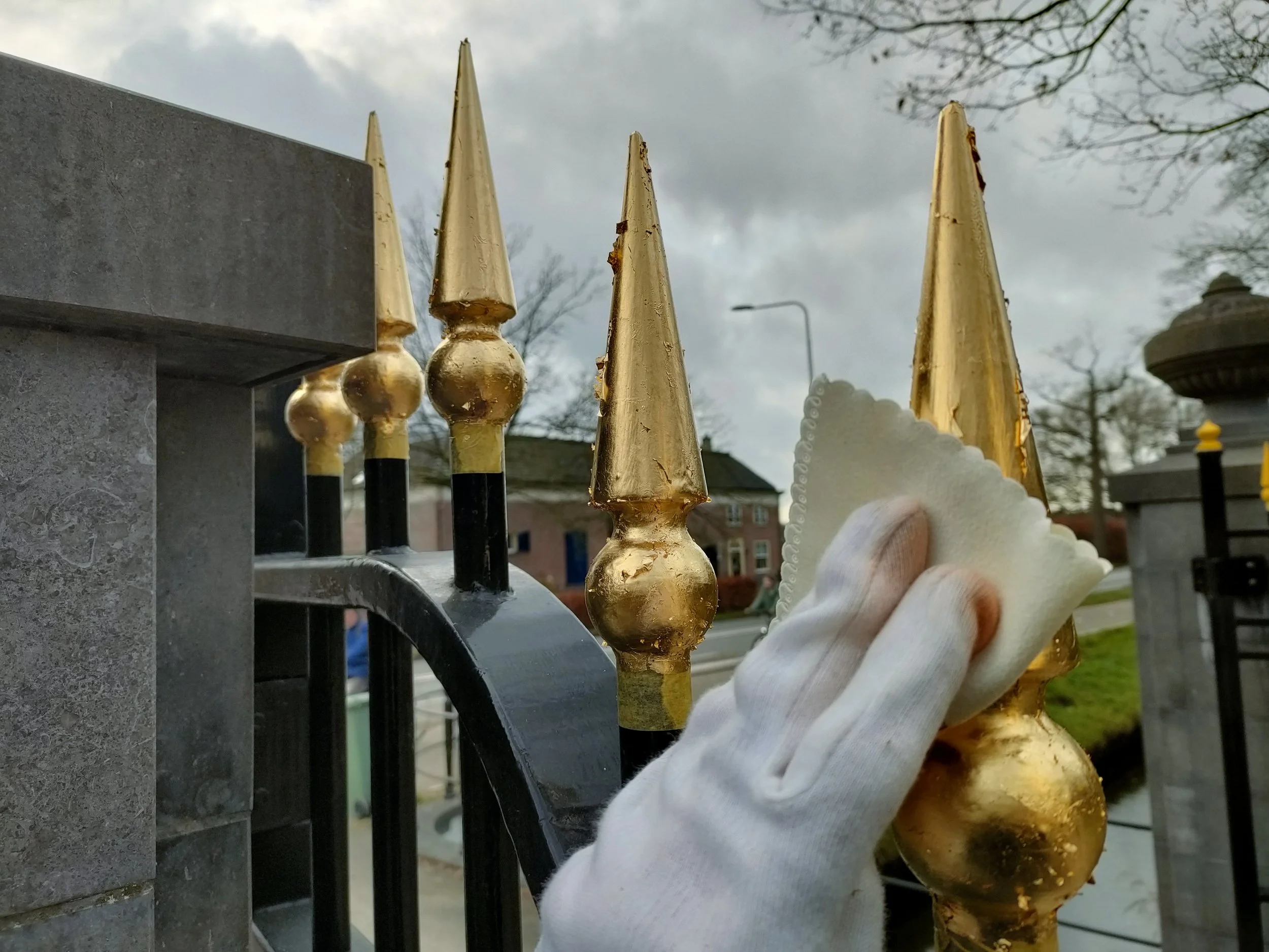 Mensen met witte handschoenen poetsen een hek met gouden spijlen.