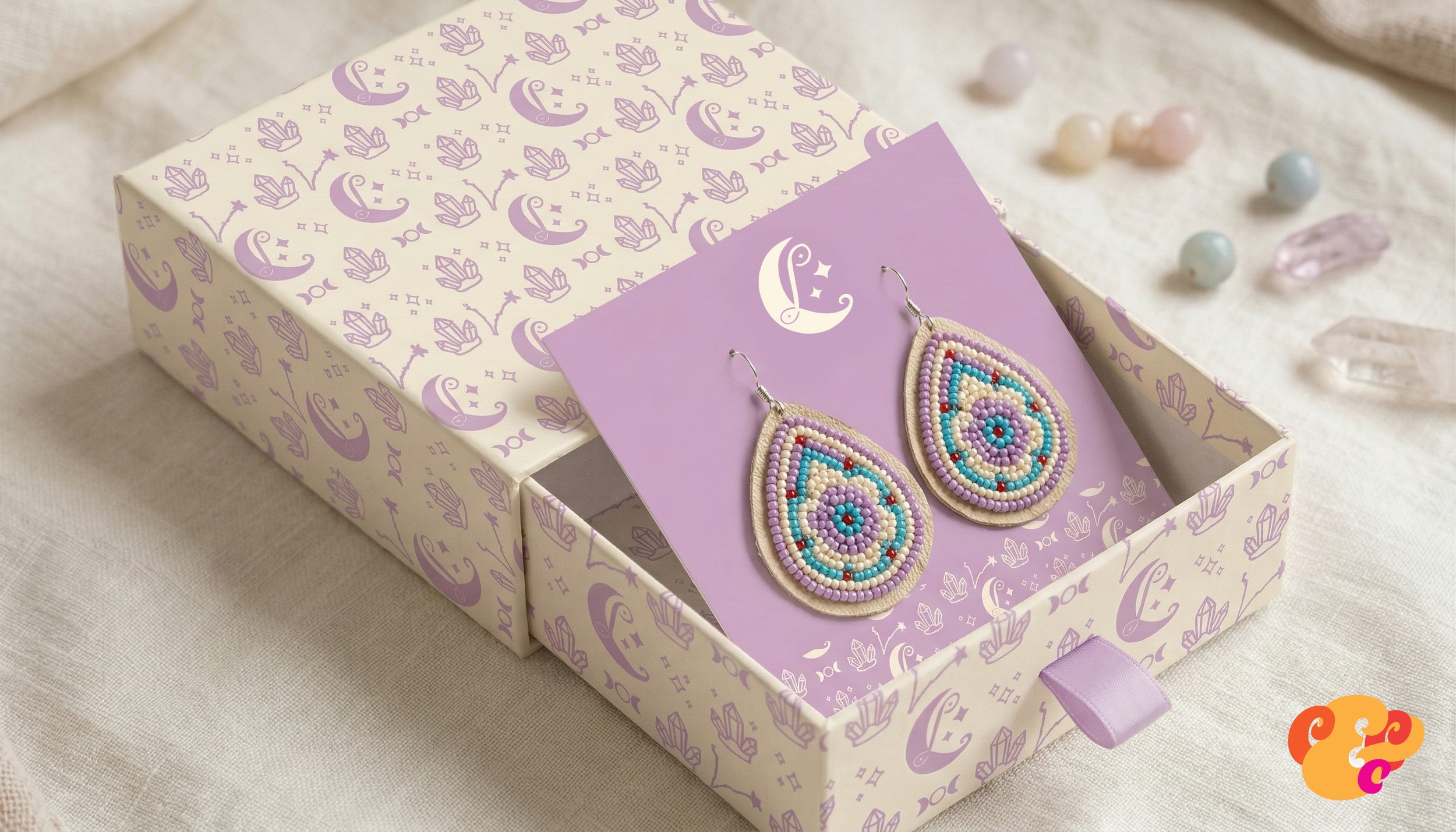 Colorful beaded tear-drop earrings on purple display card inside a decorative box with moon and star pattern.