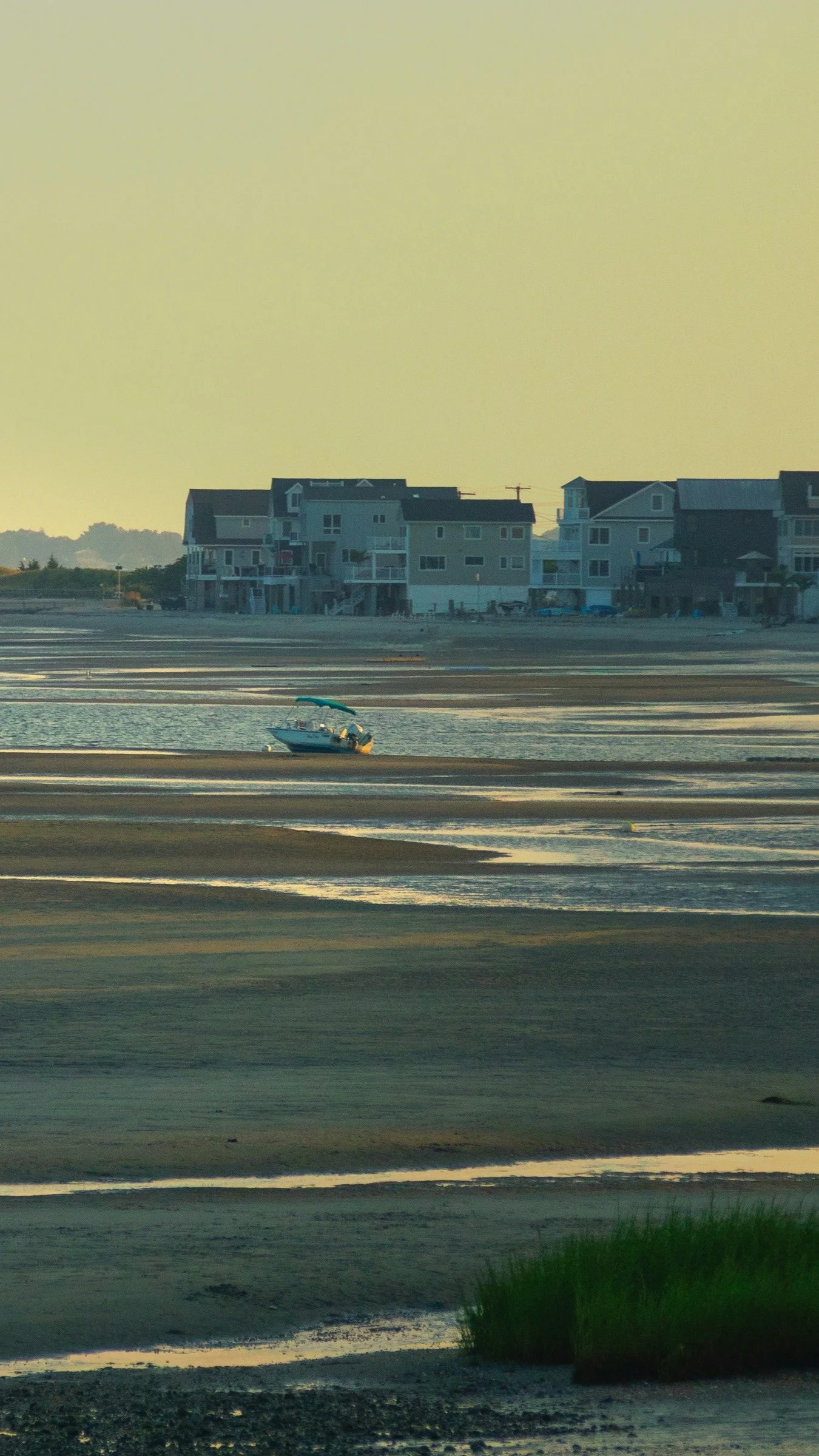 A small boat on wet sand at low tide near seaside houses with a hazy sky in the background.