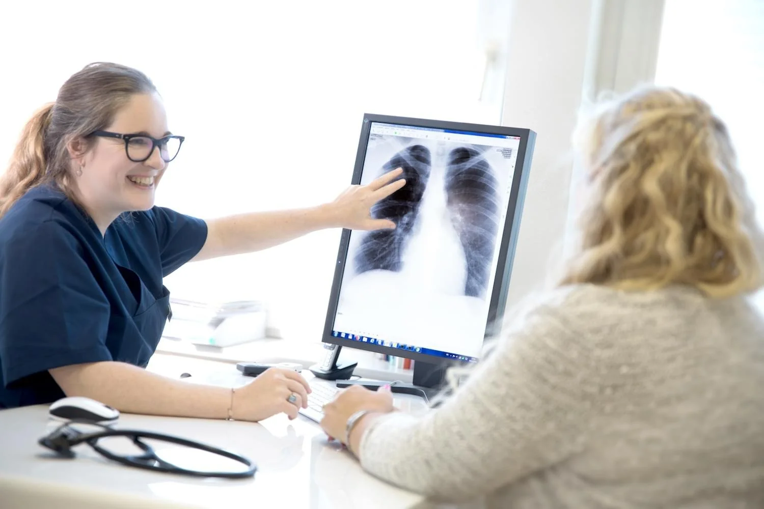Eine Ärztin zeigt einer Patientin auf einem Computerbildschirm Röntgenaufnahmen der Lunge.