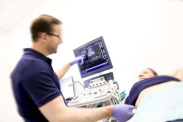 Medizinisches Personal führt eine Ultraschalluntersuchung bei einer liegenden Patientin durch.