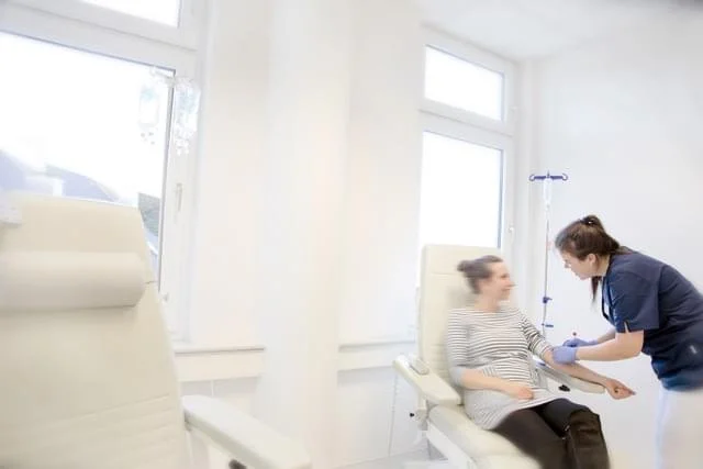 Eine medizinische Fachkraft untersucht eine sitzende Patientin im Krankenhauszimmer.