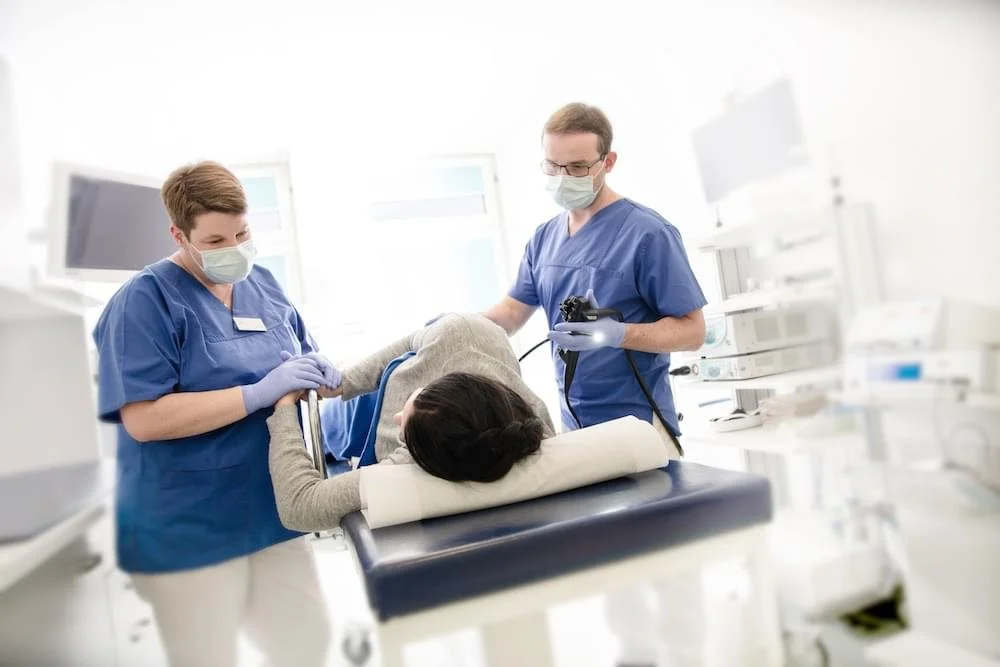 Zwei medizinische Fachkräfte bereiten einen Patienten auf eine Untersuchung in einem klinischen Raum vor.