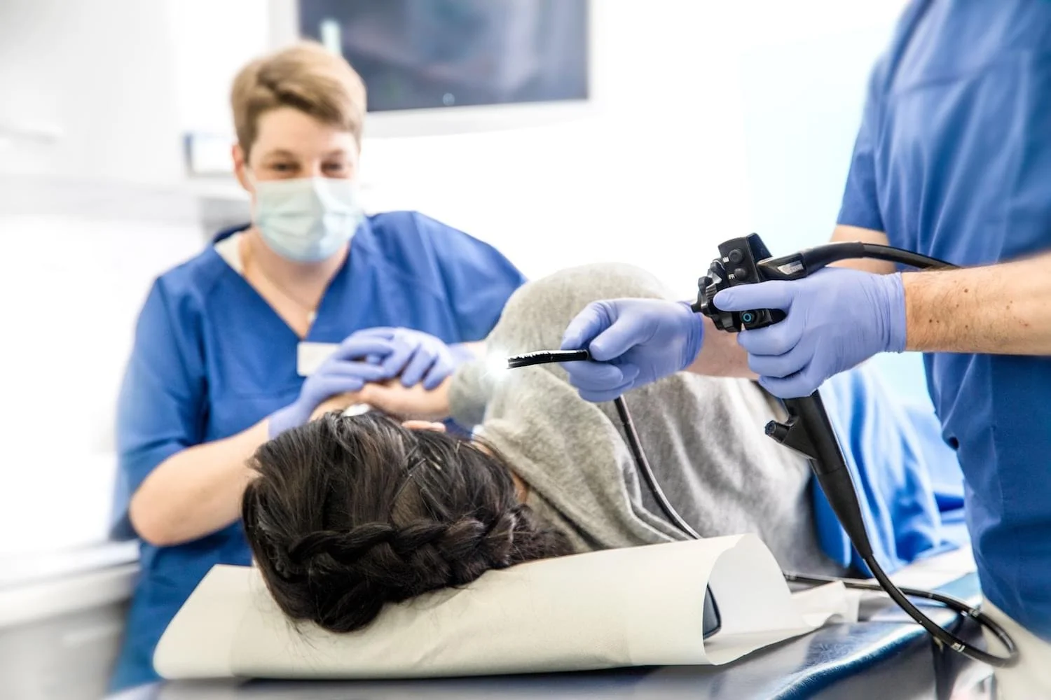 Ärztinnen oder Pflegekräfte führen eine medizinische Untersuchung bei einem liegenden Patienten durch, der auf einem Untersuchungstisch liegt, während sie Schutzmasken und Handschuhe tragen.