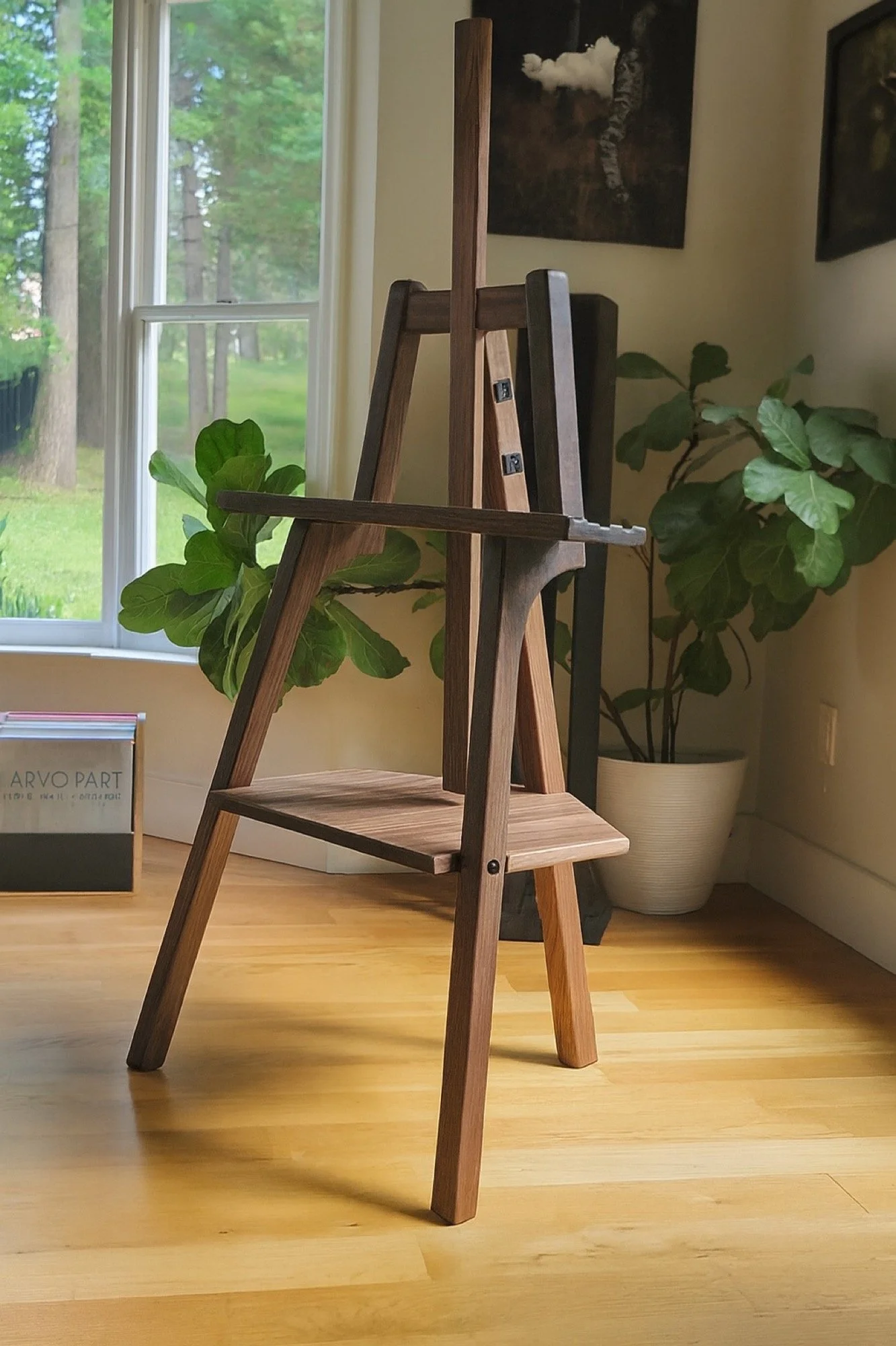 A wooden step ladder positioned inside near a window with green outdoor scenery, with houseplants and artwork on the walls.
