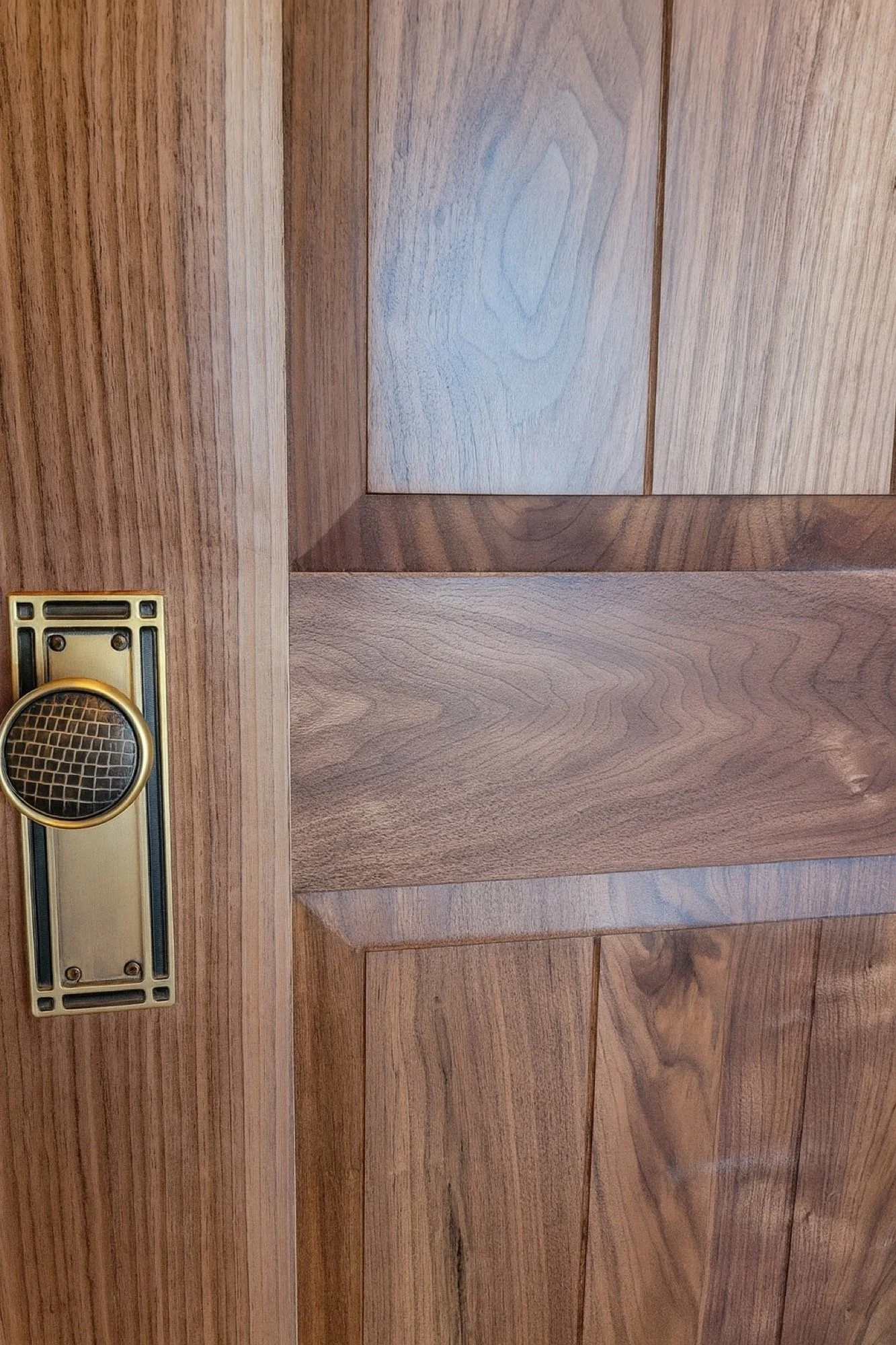 Close-up of a wooden door with a brass-colored mail slot and a round peephole.