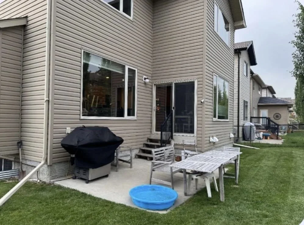 Backyard patio area with wooden table, chairs, a blue kiddie pool, grill with cover, and sliding glass door leading into house.