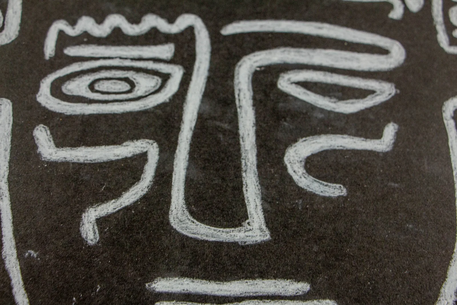 Synaptic Mythos 003 detail: frontal face, ridged brow, spiral-pupil eye and a thin mouth bar; dense white strokes on matte black with faint ghosting from double passes