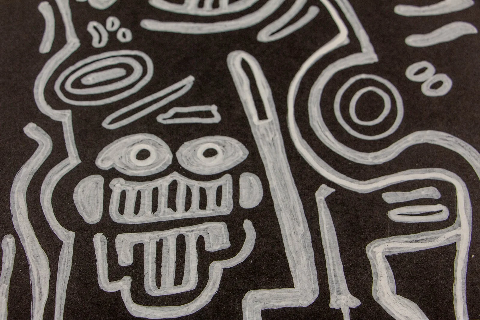 Metamorphic Entwining 003 detail: grinning side figure with picket-fence teeth and protruding tongue, round eyes and dot accents; white ink on black paper