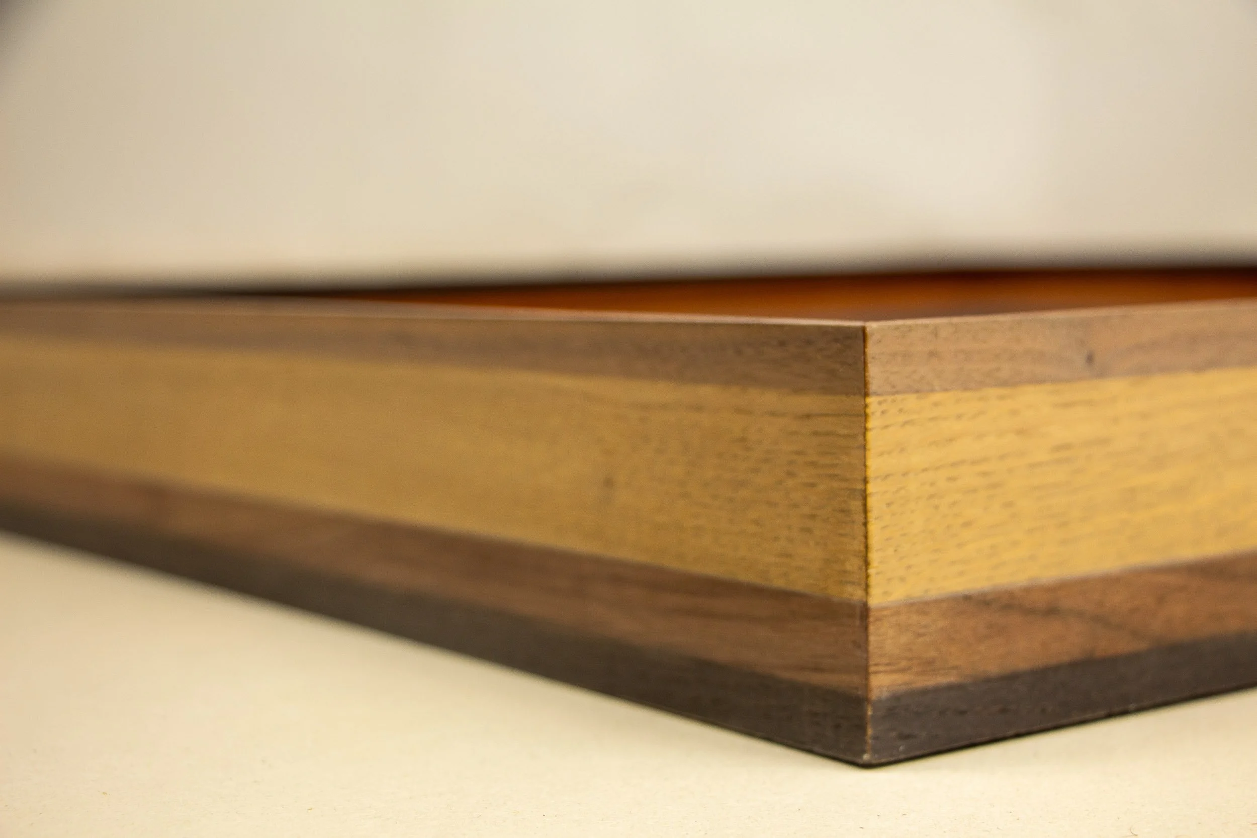 Mêlée of Discovery 001 frame: outer-corner close-up of the frame, showing the precise join and the alternating dark and lighter wood bands that give the construction its restrained wave-like rhythm.