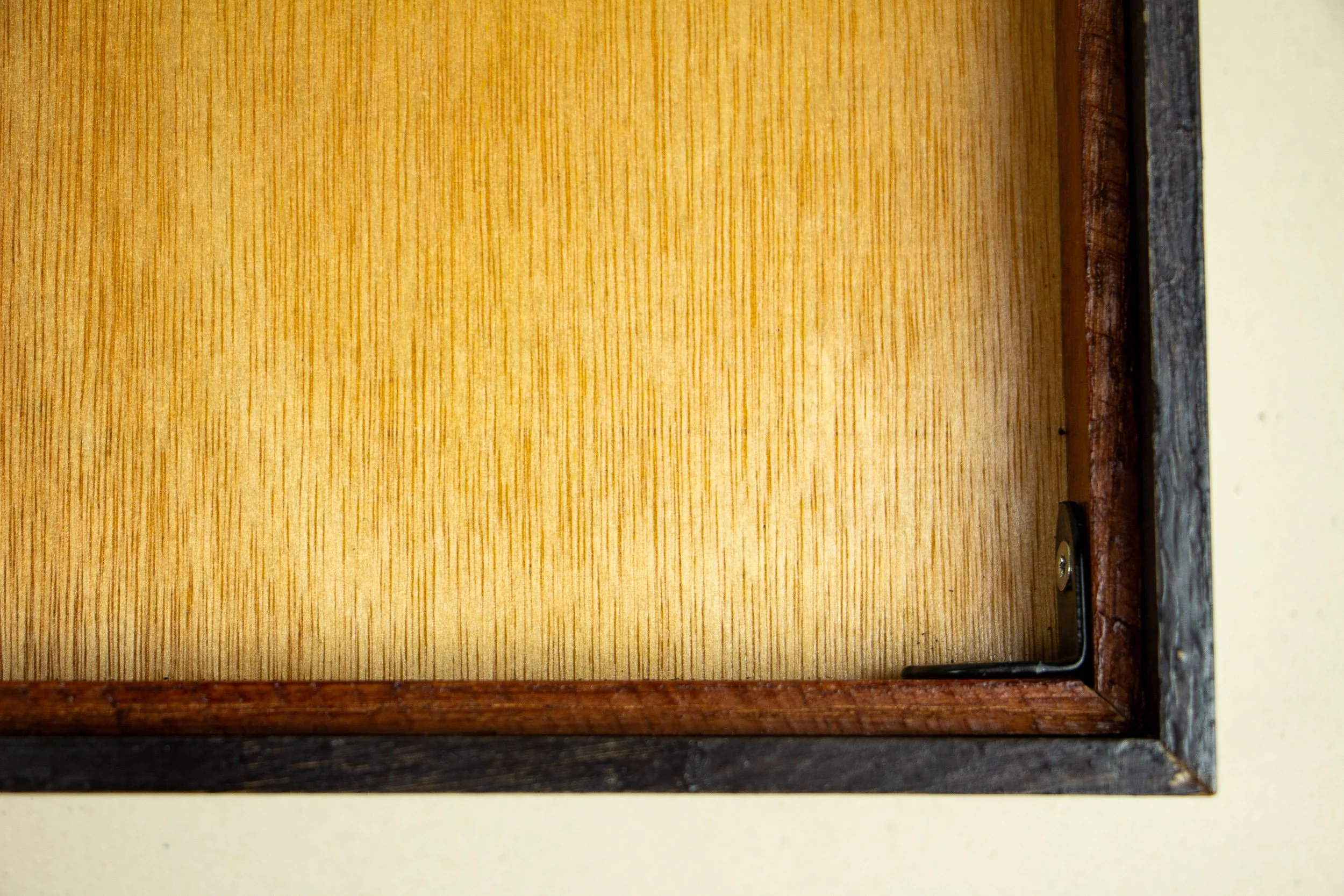 Mêlée of Discovery 005 frame detail: close-up of the reverse inner corner, showing the warm-toned back panel, dark outer frame edge, and black metal corner bracket securing the construction.