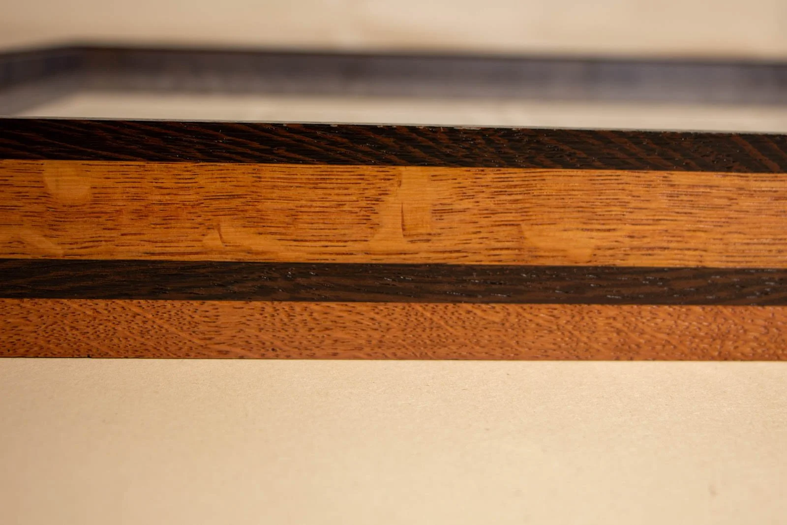Formless Equation Artwork 003 frame detail: layered oak profile with wenge top edge and mid-band, warm honey/brown tones, linear grain clearly visible.