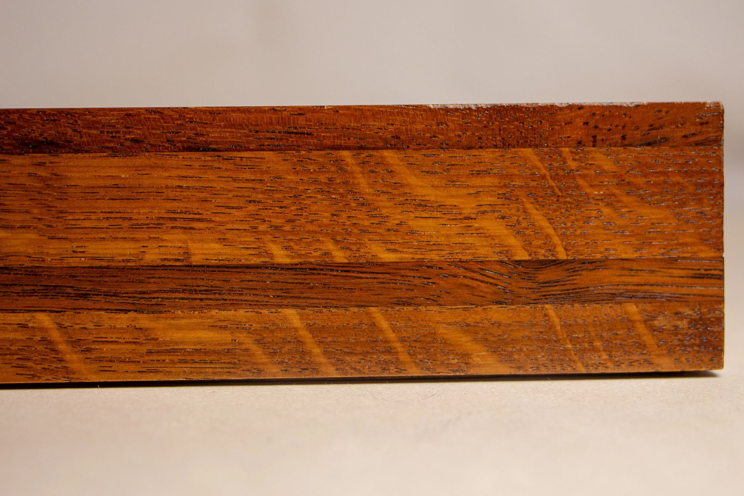 Turbulent Aegis 003 frame detail: close-up of the frame side showing the warm amber-brown wood, darker central band, and pronounced grain pattern that give the frame depth, rhythm, and visual weight