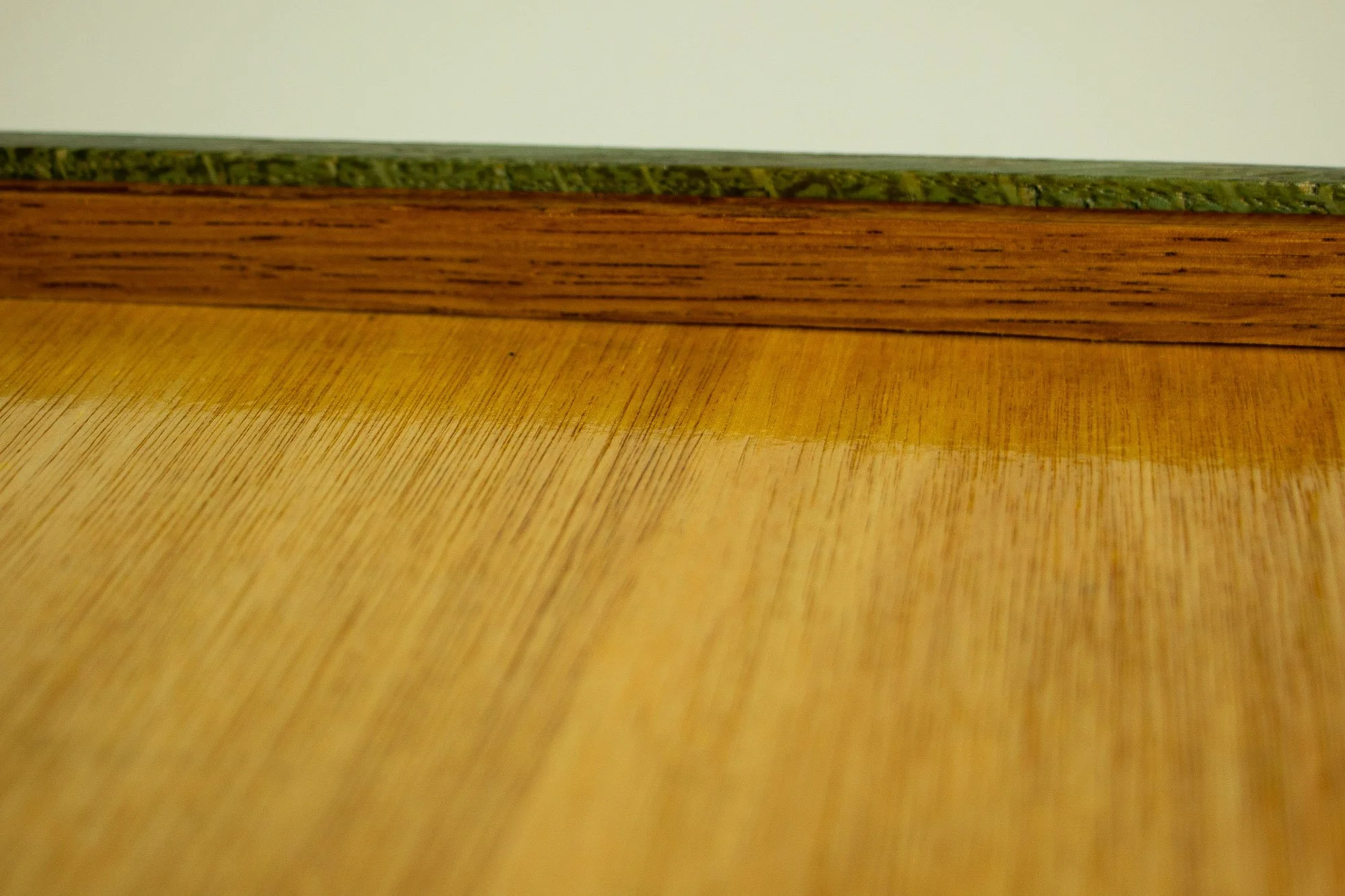 Eclipsing Gravitas 001 frame: overhead reverse-side corner detail showing the meranti plywood back panel, green-toned inner rim, outer oak edge, and black metal corner brace fixed into the frame.