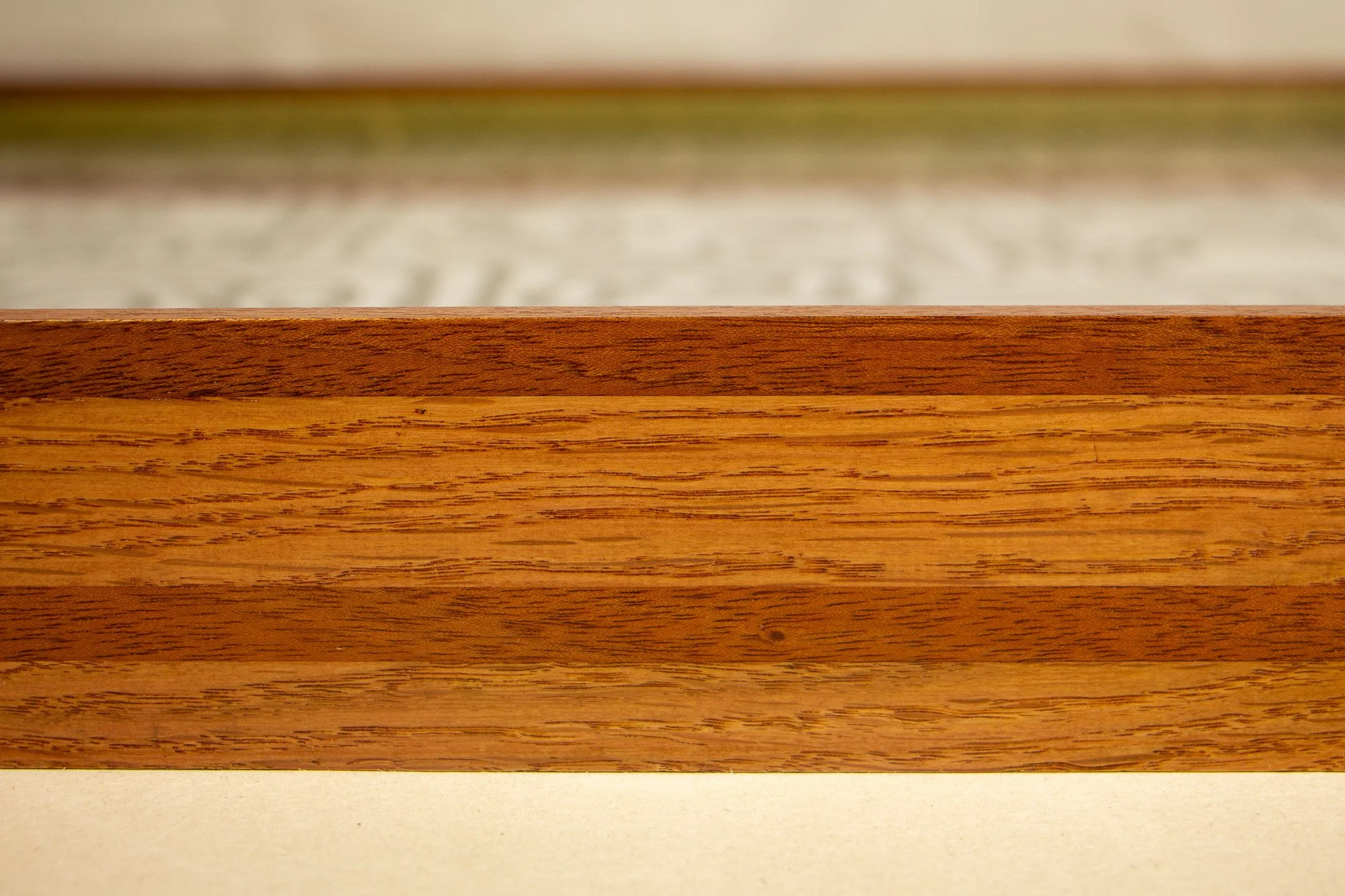 Resonant Syntax 001 frame: horizontal close-up of the frame profile, showing layered mahogany and oak elements in a pink, mint, and blue sequence with visible natural grain