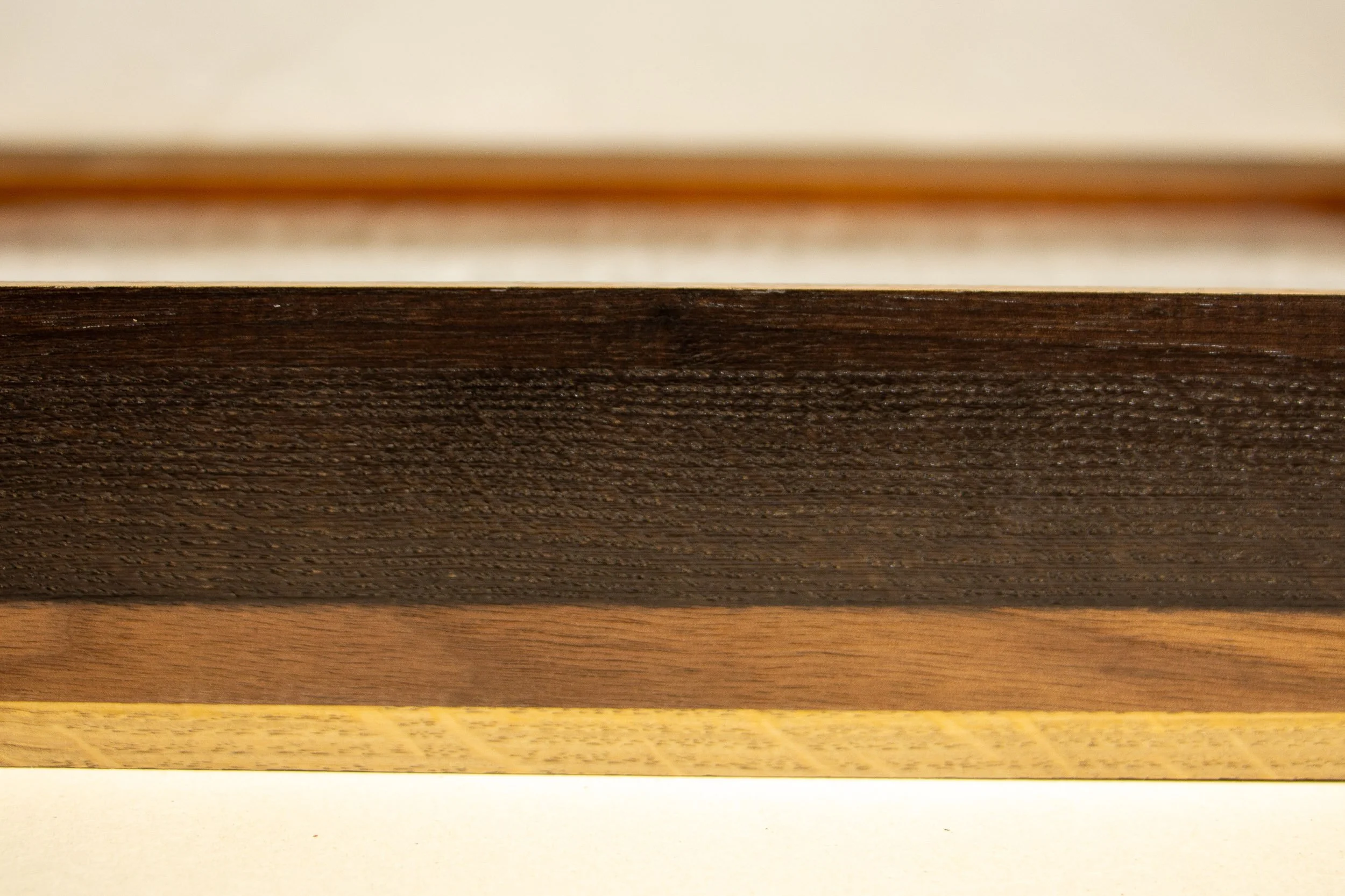 Mêlée of Discovery 002 frame: side detail of the frame profile, emphasizing the stratified wood bands and the subtle contrast between dark containment, warm mid-tone, and lighter base.