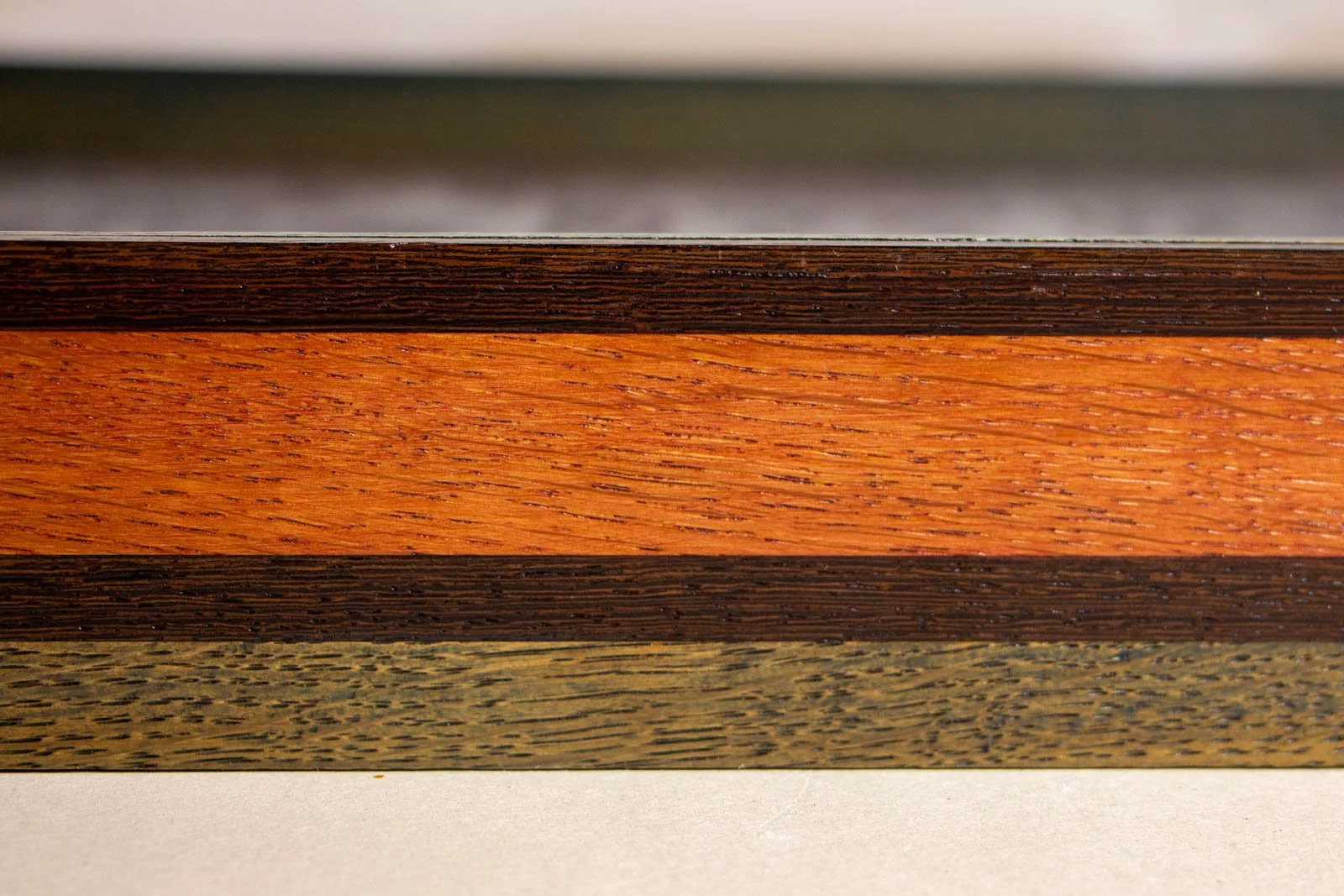 Silence’s Caesura 002 frame: side panorama, mahogany band held between the wengé shadowline above and the cool oak below; soft reflections along the edge