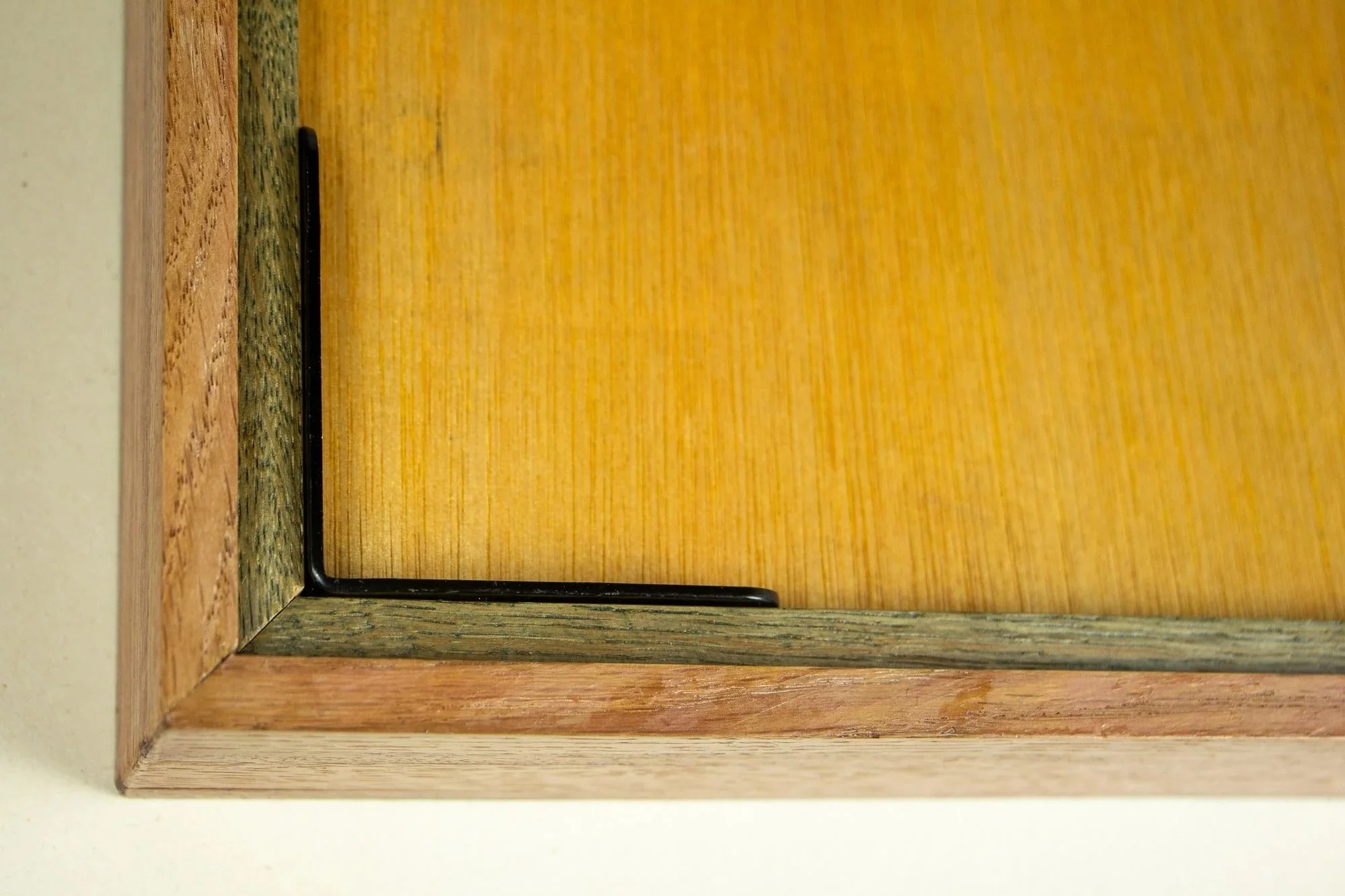 Resonant Syntax 001 frame: reverse corner detail of the frame construction, showing the meranti plywood back panel, black metal corner bracket, layered oak structure, and mahogany outer edge