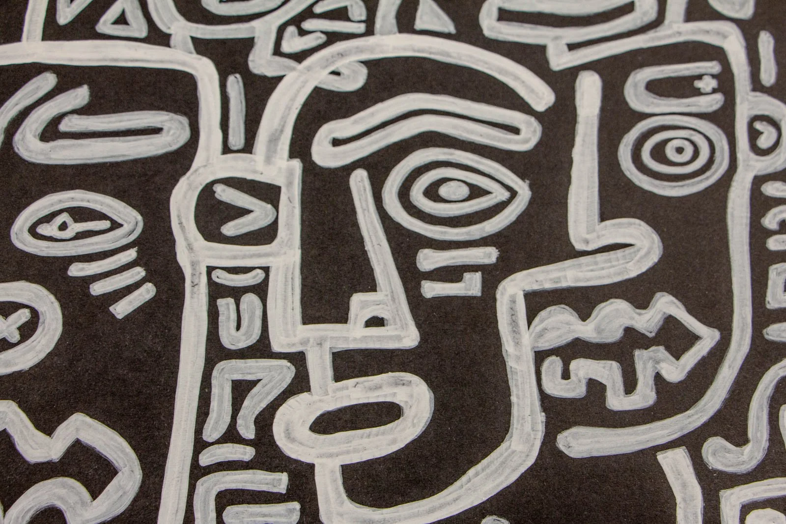 Metamorphic Entwining 002 detail: central long-nose head with concentric eye and oval lips, neighbor showing triangular teeth, confident contour lines, white ink on black paper